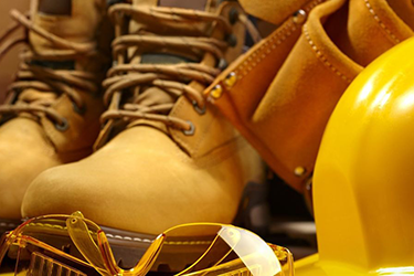 picture of workplace saftey gear includes hard hat, gloves, boots and safety glasses.