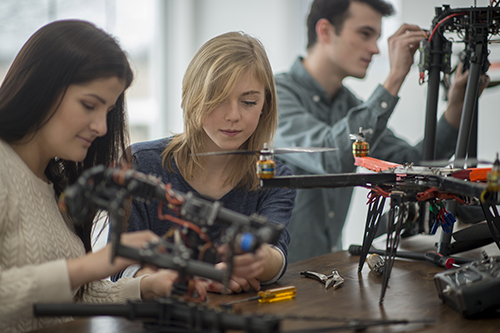 A group of college students are working on the mechanics for a robotics and drone project in university.